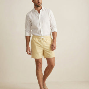 Apprivió Lumari swim shorts in light yellow worn with white linen shirt, full body look.