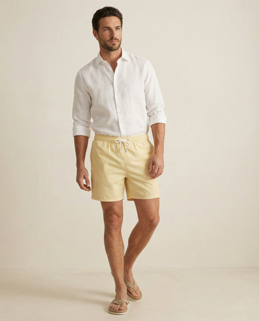 Apprivió Lumari swim shorts in light yellow worn with white linen shirt, full body look.