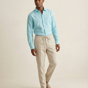 Men’s Noya natural linen trousers worn with light blue linen shirt, full outfit view
