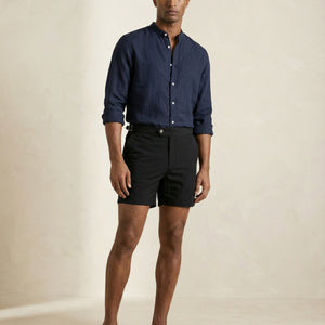 Model wearing Apprivió Riviera black tailored swim shorts with side buckle waistband and linen shirt.